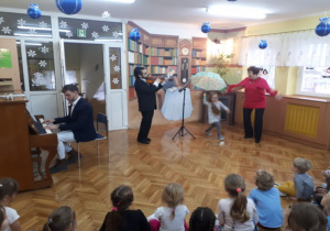 Muzycy grajacy na instrumentach, dziewczynka z parsolką tańczy z prowadzacą audycję.